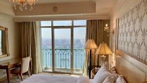 A hotel room with a large bed, a desk, and a view of the city through the balcony doors.