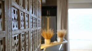 Une pièce avec un mur décoratif en panneaux de bois, une petite étagère ornée de plantes séchées et un aperçu d’un lit avec une tête de lit blanche.