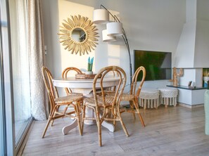 Un comedor con una mesa redonda, cuatro sillas de mimbre, un espejo con forma de sol montado en la pared y una lámpara moderna.