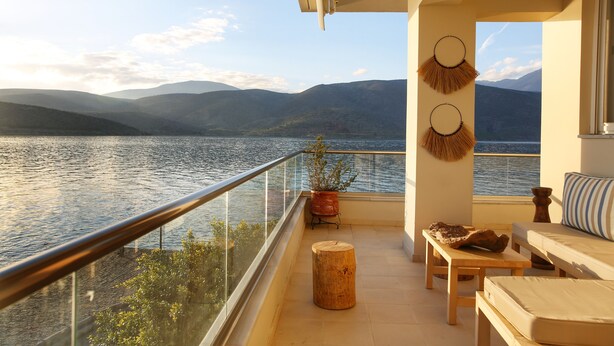 Un balcon offrant une vue sur un lac et des montagnes, aménagé avec un canapé, une table et une plante en pot.