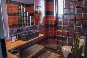 Un baño con tocador de madera, lavamanos, espejo, inodoro y zona de ducha.