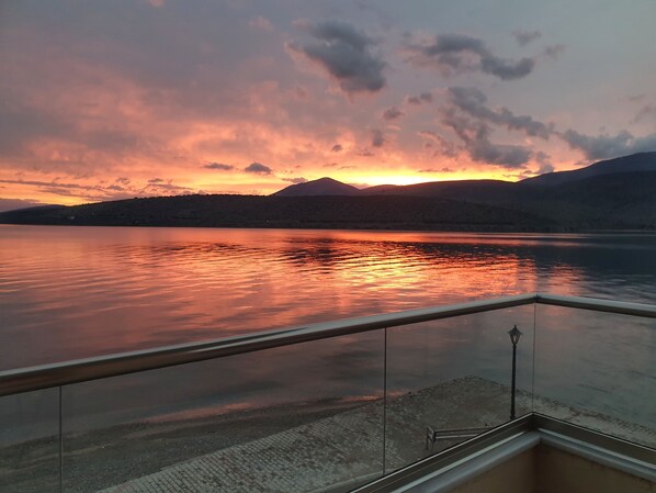 A lake with a sunset view, a balcony with a railing, and a mountain in the background.