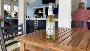 A bottle of Sands Light beer on a wooden table in a restaurant with blue walls and a TV mounted on the wall. - Stunning Oceanfront Condo at Coral Beach unit 1107 (Freeport)