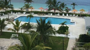A pool area with palm trees, lounge chairs, and umbrellas. - Stunning Oceanfront Condo at Coral Beach unit 1107 (Freeport)