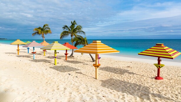 A beach with multiple colorful striped umbrellas and palm trees. - Stunning Oceanfront Condo at Coral Beach unit 1107 (Freeport)