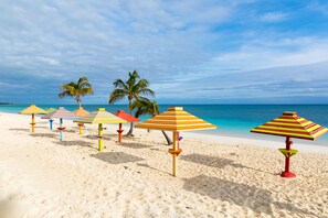 A beach with multiple colorful striped umbrellas and palm trees. - Stunning Oceanfront Condo at Coral Beach unit 1107 (Freeport)