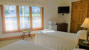 Quarto de hotel com duas camas, uma televisão na parede, uma porta de madeira e uma janela com persianas.