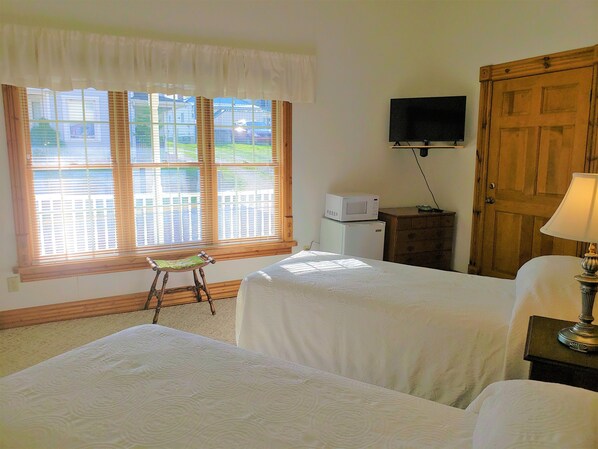 A hotel room with two beds, a television on the wall, a wooden door, and a window with blinds. - Historic Hardware Inn with River Views: Suite 102 (Stockport)