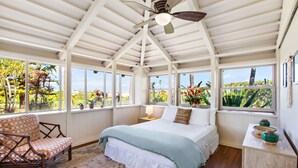 Un dormitorio con cama, una silla, una mesita de noche y una ventana que ofrece vistas al verdor.