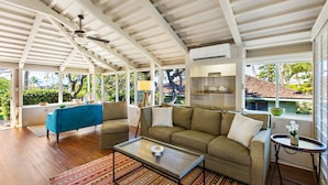 Una habitación amplia con techo alto, ventilador de techo, sofá, mesa de centro y vistas a una piscina y zonas verdes.