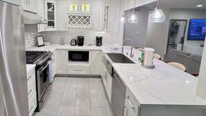 A modern kitchen with white cabinets, a built-in oven, a microwave, and a sink. There are pendant lights above the counter and a large window above the sink. - Rainforest 4BR Pool Villa - Walk to Disneyland (Anaheim)