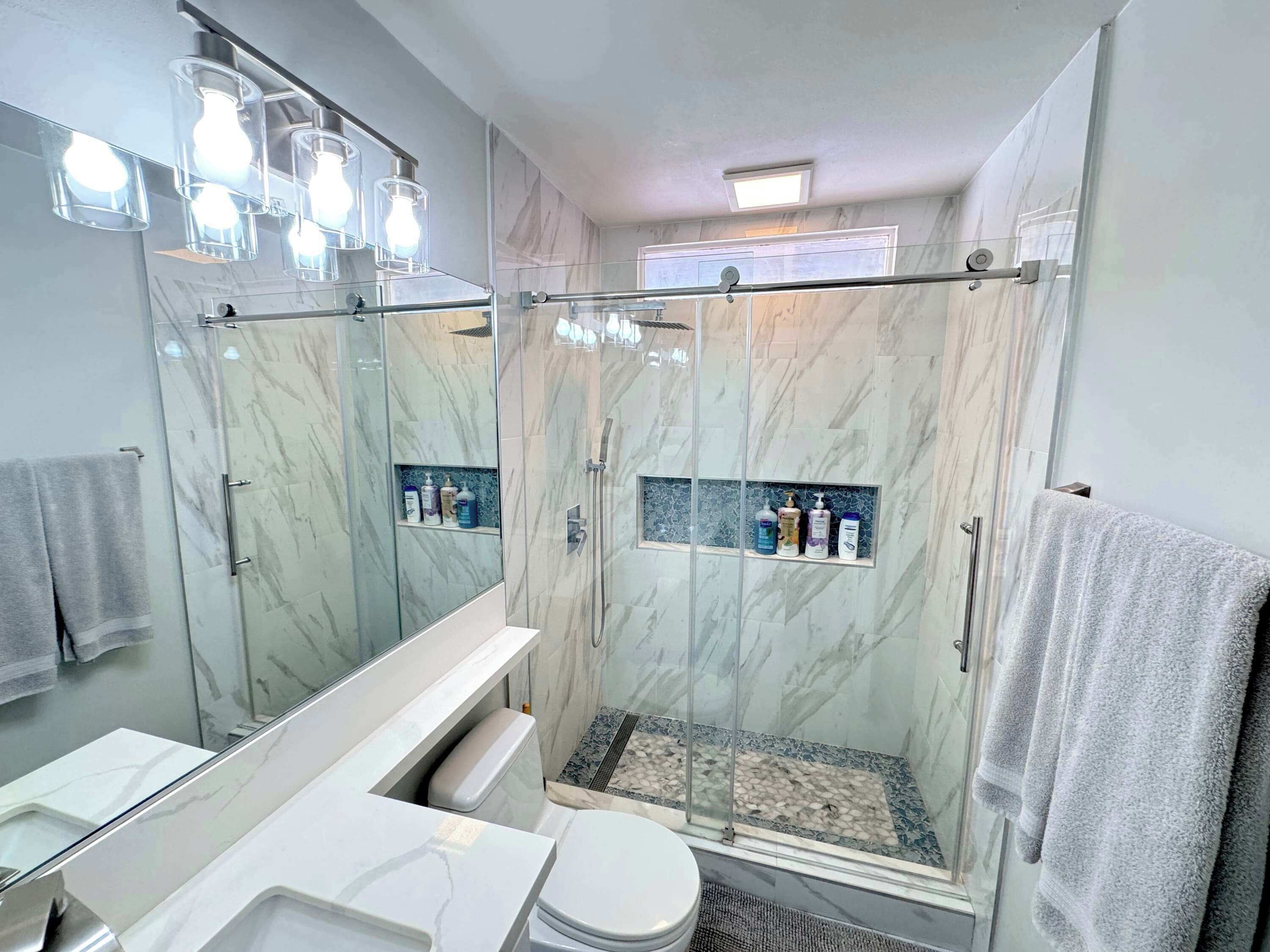 A modern bathroom with a glass-enclosed shower, marble walls, and a vanity with a mirror.