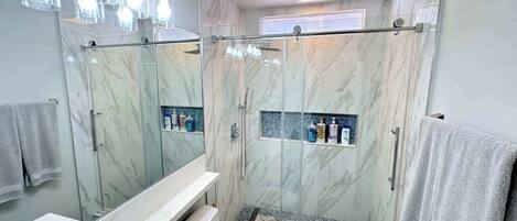 A modern bathroom with a glass-enclosed shower, marble walls, and a vanity with a mirror.