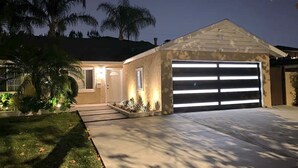 A two-story house with a garage, a well-lit entrance, and a landscaped front yard. - Rainforest 4BR Pool Villa - Walk to Disneyland (Anaheim)