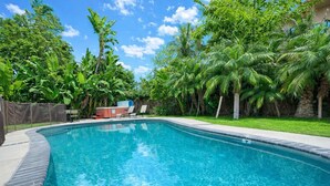 A clear blue swimming pool surrounded by lush greenery and palm trees. - Rainforest 4BR Pool Villa - Walk to Disneyland (Anaheim)