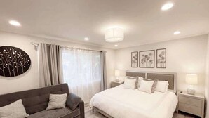 A modern bedroom with a large bed, a dark sofa, and a round wall decoration. - Rainforest 4BR Pool Villa - Walk to Disneyland (Anaheim)