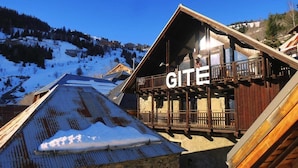 Un edificio de madera con balcón y la palabra 'GITE' en su fachada, rodeado de montañas nevadas.