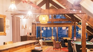 Un espacio interior acogedor con mesa de billar, mobiliario de madera y un amplio ventanal con adornos de estrellas.