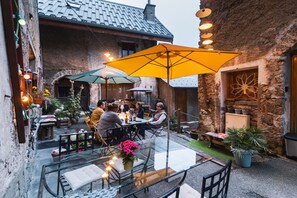 An outdoor dining area with tables and chairs, surrounded by stone walls and potted plants. - Gîte Auris (Auris)