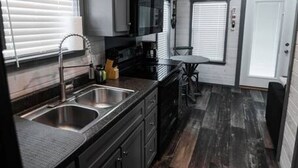 A compact kitchen with dark wood cabinets, a stainless steel sink, and a microwave.