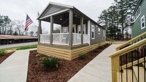 A single-story house with a covered porch, a front yard with mulch and small plants, and a visible American flag.