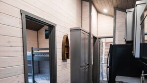 A narrow hallway with wooden walls, a bunk bed, a trash bin, and a kitchen area with a sink and cabinets.