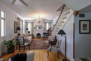 Cozy living room with a fireplace, grand piano, and staircase leading to an upper level, offering a comfortable seating area with a sofa and armchairs.