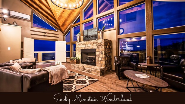 A cozy lounge area with a stone fireplace, leather seating, and large windows offering a view of the night sky. - Gorgeous Luxury Cabin! 360 Views, Fire Pit, Theater Room - Prime Location!  (Gatlinburg)