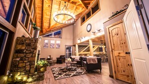 A spacious living area with a stone fireplace, wooden ceiling beams, and a large chandelier. - Gorgeous Luxury Cabin! 360 Views, Fire Pit, Theater Room - Prime Location!  (Gatlinburg)