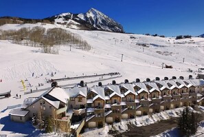 A snow-covered mountain with a ski resort in the foreground, featuring a row of chalet-style buildings with a ski lift visible.