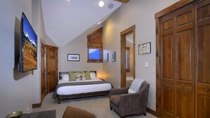 Ein Schlafzimmer mit einem Bett, einem Sessel, einem Fernseher und Holztüren.