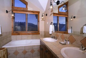 A bathroom with a bathtub, two sinks, wooden window frames, and wall-mounted lights. - Silver Ridge 3 (Crested Butte)