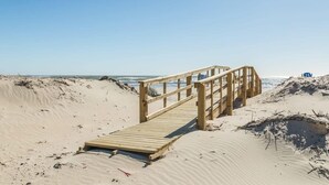 Una passerella di legno conduce a una spiaggia con dune sabbiose e l'oceano sullo sfondo.