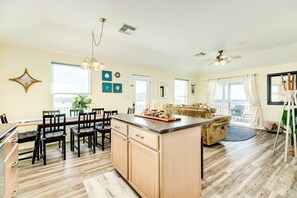 A spacious kitchen with a central island, wooden cabinets, and a dining area with chairs and a table. - Sunset Sanctuary - Yep, Coolest Sunrises & Sunsets Here! (Surfside Beach)