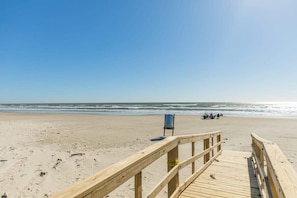 Una pasarela de madera que lleva a una playa, con una silla y un carrito de golf a lo lejos.