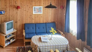A cozy cabin interior with a blue patterned sofa, a small table with a checkered tablecloth, a television on a wooden stand, and a window with curtains. - Awesome home in Spangereid with kitchen (Spangereid)
