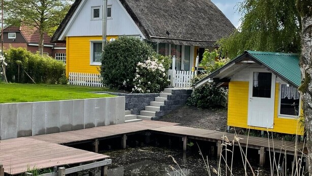 Une maison avec un toit de chaume, une antenne parabolique et un petit quai qui s’avance dans l’eau.