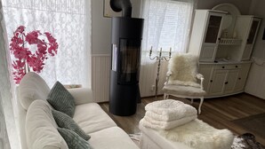 Un salon chaleureux avec un canapé blanc, un fauteuil moelleux, un meuble blanc et un poêle à bois.