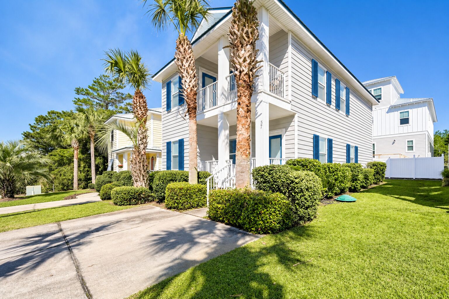 A two-story house with a front porch, palm trees, and a well-maintained lawn.