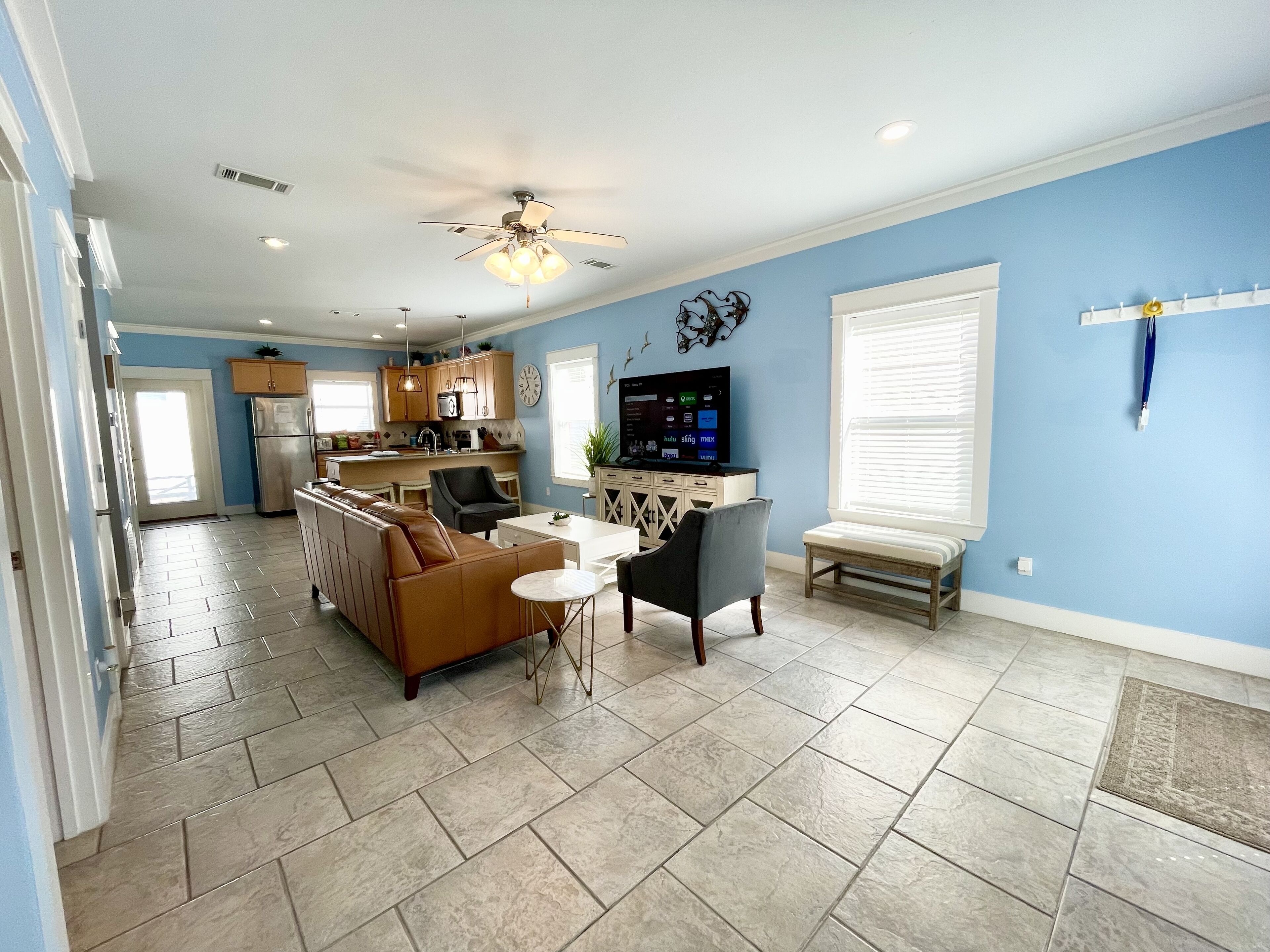 A modern kitchen with a built-in oven, a dining area with a brown leather couch and a small round table, and a living room with a flat-screen TV.