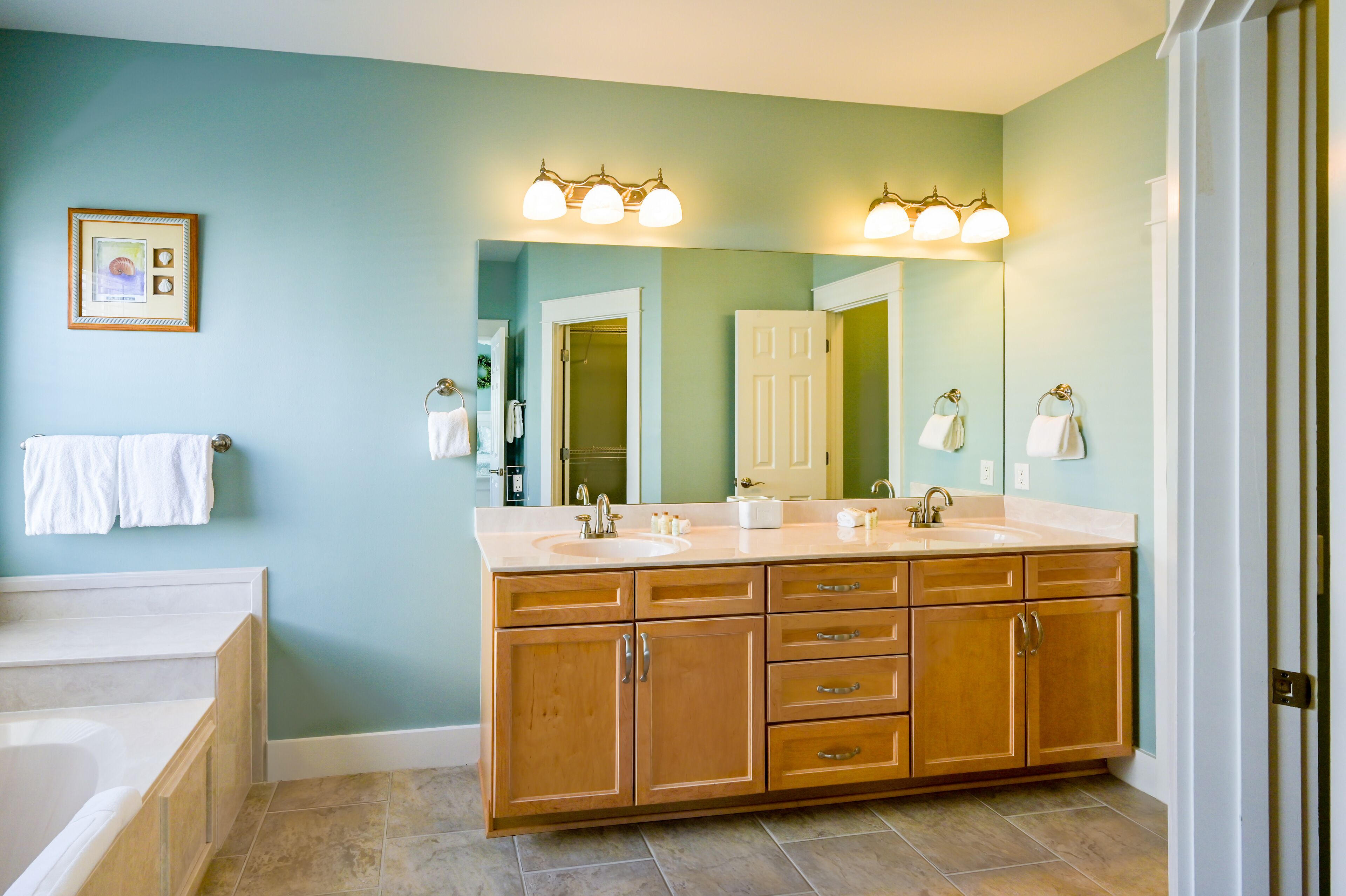 A bathroom with a double sink vanity, a large mirror, and a bathtub.
