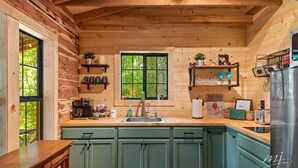Eine Küche mit Holzwänden, einem Spülbecken und Schränken. Regale mit Gegenständen und ein Fenster mit Blick auf Bäume.