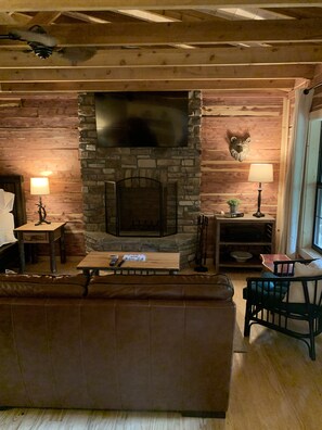 A cozy living room with a stone fireplace, wooden walls, a leather sofa, and a wooden coffee table.