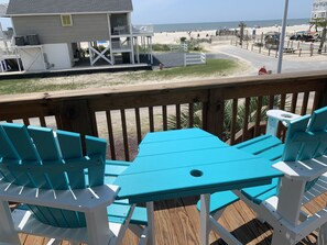 A deck with turquoise chairs and a table overlooking a beach.