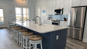 Een moderne keuken met witte kasten, een roestvrijstalen koelkast en een groot kookeiland met barkrukken.