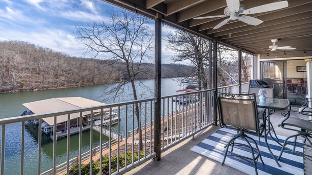 A covered outdoor deck with a view of a lake, a boat dock, and a dining area with chairs and a table. - Unit B7 spacious 4bed/3bath condo perfect lakefront spot for family and friends (Osage Beach)