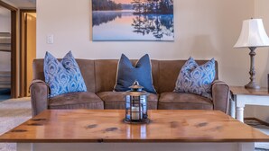 A living room with a brown sofa, patterned cushions, a wooden coffee table, a floor lamp, and a painting of a lake. - Unit B7 spacious 4bed/3bath condo perfect lakefront spot for family and friends (Osage Beach)