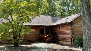 Une cabane en rondins avec une façade en bois, un porche et une allée gravillonnée.