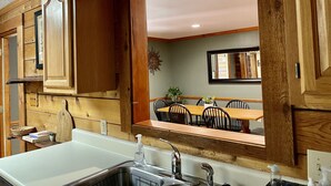 Une cuisine avec des meubles en bois, un plan de travail blanc et un coin repas visible à travers une porte ouverte.