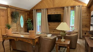 L’intérieur d’un chalet confortable, avec un plafond en bois, un téléviseur à écran plat fixé au mur, un canapé, une table basse et une lampe.
